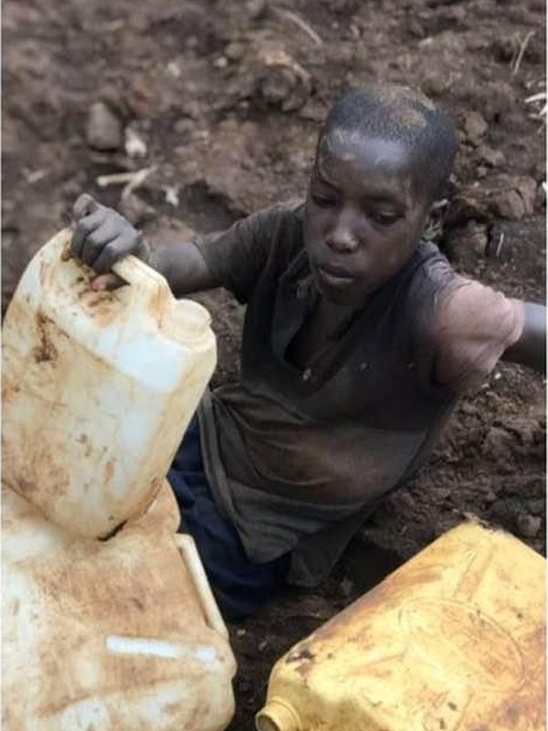 A boy collecting water in yellow jerrycans from a muddy hole in the ground