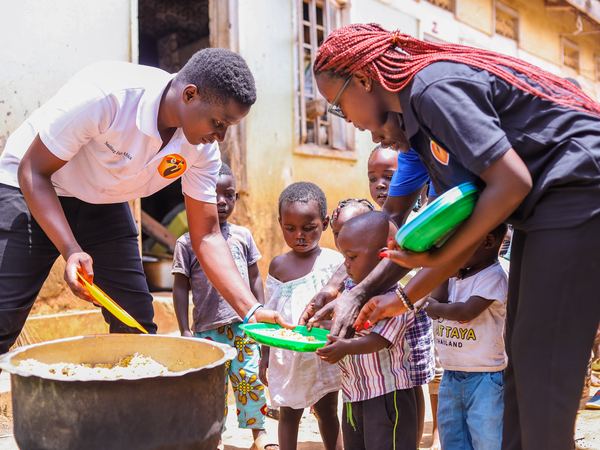 Our team serving food from a large pot as children wait with plates