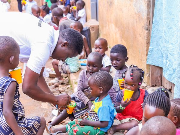 A volunteer kneeling to serve drinks to young children sitting in a row
