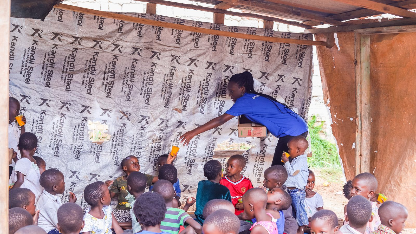 A volunteer serving drinks to a crowd of children under a shelter