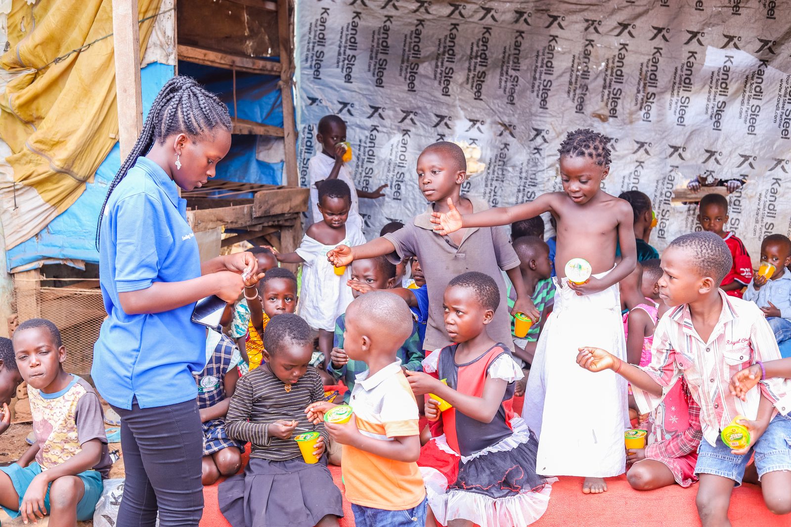 A volunteer handing out drinks to children sitting together for a meal