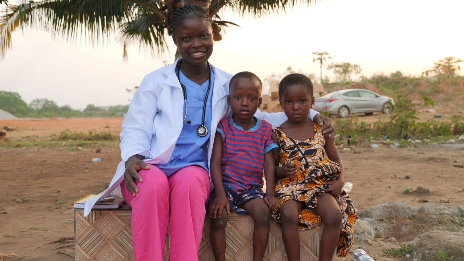A health worker sitting with two children outdoors